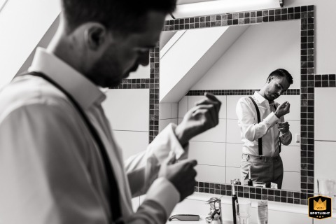 In an Austrian hotel room, the groom fixes his cufflinks, captured in a black-and-white image of him reflected in the bathroom mirror while preparing for the wedding.