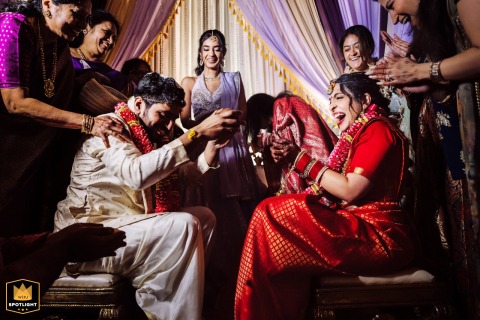 At Virginia's Riverside on the Potomac, the bride and groom participate in an intimate indoor ritual, seated face to face and surrounded by family members laughing joyfully.