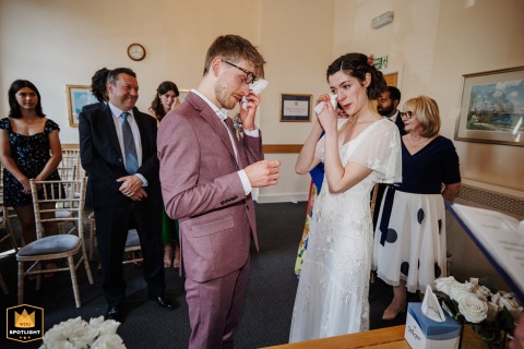 At Beaconsfield Registry Office, the bride and groom, overcome with emotion during their wedding ceremony, gently wipe tears from their cheeks, sharing a touching and heartfelt moment as they exchange vows.
