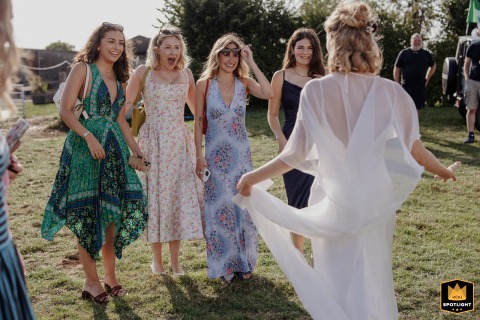 At a St Albans reception venue in Hertfordshire, friends joyfully see the bride for the first time outside on the grass, sunlight behind them illuminating her and capturing genuine excitement and happiness.