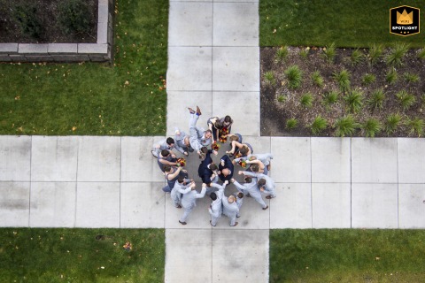 At the Walker Museum of Art in Minneapolis, MN, a drone captures the entire wedding party converging around the couple at a sidewalk intersection, creating a dynamic and celebratory aerial scene of urban togetherness.