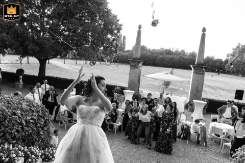 At Villa Schiarino in Bancole, Mantua, Italy, the bride tosses her bouquet from the staircase. The bouquet hovers humorously between two grand columns, resembling a goal, adding playful energy to the elegant setting. 