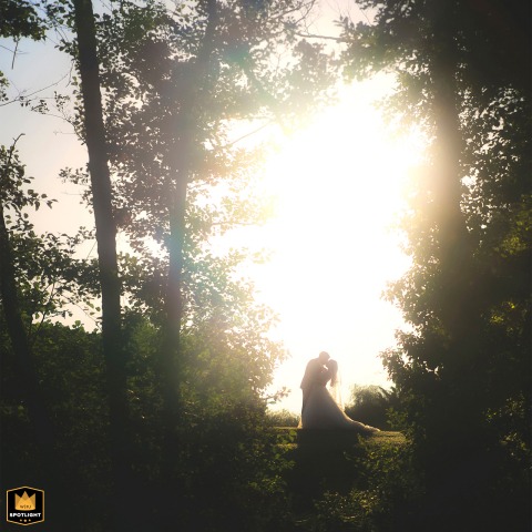 In Dordogne, France, two lovers share a gentle kiss in profile at sunset, the groom dipping his partner slightly. They are beautifully framed by trees, with the golden sun glowing behind them.
