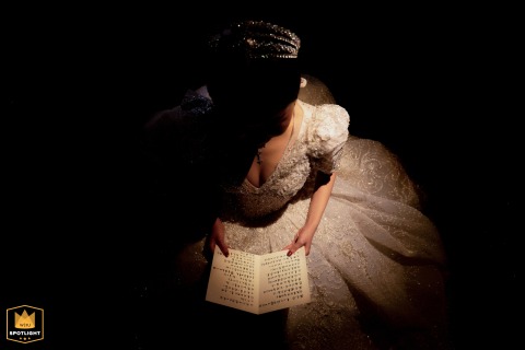 In a Taiyuan, Shanxi hotel, dramatic lighting highlights the bride as she reviews her handwritten vow card from a top-down angle, capturing quiet reflection and anticipation just before the wedding ceremony.