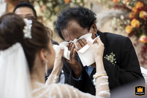At W Bangkok, the father of the bride wipes his eyes with a kerchief, visibly moved, as the bride gently adds two more tissues to help, highlighting the deep bond and shared emotions of the day.