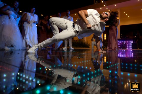 In Avignon, a stylish man wearing sunglasses shows off his breakdancing skills on the dance floor, striking a dynamic pose as onlookers watch, capturing the vibrant energy and fun of the celebration.