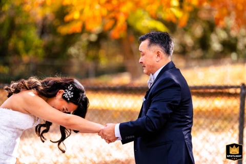 Outside the Mansion on Main Street in New Jersey, a father tightly holds his daughter’s hands, both shedding tears as they navigate the emotional farewell, surrounded by the colors and crisp air of a fall wedding setting.