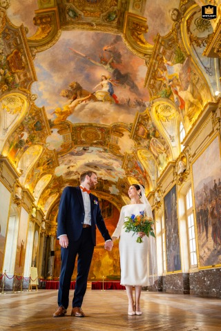 Inside the Salle des Illustres at Toulouse City Hall, this low-angle vertical shot features the bride and groom standing together, highlighting the grandeur of the ornate space and capturing the significance of their wedding ceremony.