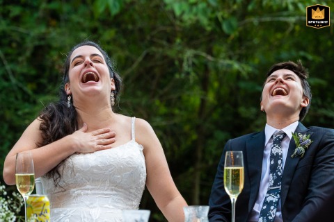 Atlanta Couple Laughing With Heads Back During Wedding Speeches Outdoors In the backyard of a home in Atlanta, Georgia, the couple sits at the head table during wedding speeches, laughing together with their heads tilted back, capturing their shared joy and the lively, relaxed atmosphere of the celebration.