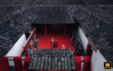 In Fujian, China, the bride and groom celebrate their marriage at home, seen from a high angle above traditional tiled rooftops, with a vibrant red carpet running beneath their feet, symbolizing happiness and cultural tradition.