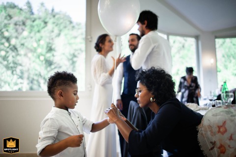At Terme di Vallio in Vallio Terme, a guest ties a balloon to a child’s wrist while, in the background, the bride and groom chat with other guests, highlighting a festive and interactive scene during the celebration.