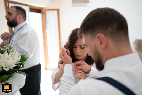 At the bride’s house in Mondragone, Italy, she assists one brother with his cufflinks while, in the background, her other brother adjusts his tie, capturing a candid and heartfelt family preparation scene before the wedding.