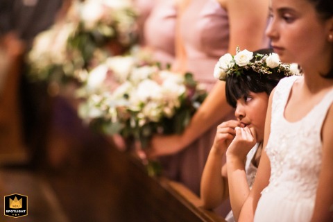 At St. Michael Catholic Church in Livermore, California, two young flower girls stand in the front row at the edge of the bridesmaids, all holding flowers during the ceremony.