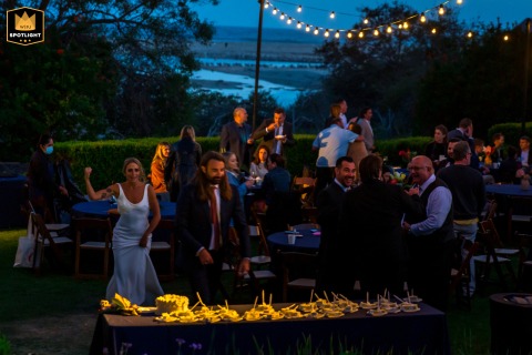 At Malibu State Park in Malibu, California, the bride and groom dash excitedly toward the dessert table as dusk settles, with glowing strings of warm lights suspended above, capturing their joyful anticipation and the enchanting outdoor celebration.