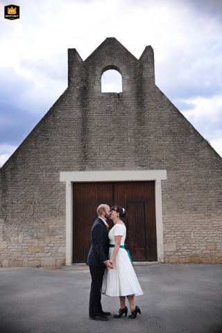   Outside Normandy, France, the bride and groom share a quick, loving kiss before heading into their wedding reception dinner, savoring a private kiss together.