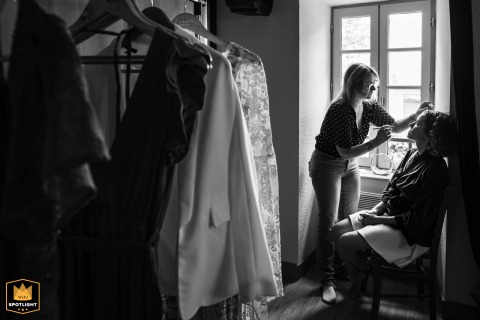 Makeup Artist Finishes Bridal Look In Window Light At Le Cruzeau In Dordogne, France In a sunlit room at Le Cruzeau, Gîte Village, Dordogne, France, a makeup artist carefully completes the bride’s look beside the window, capturing a calm preparation moment.