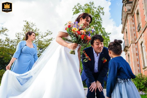 Couple Pauses Before Ceremony As Dress Is Adjusted In Limoges, France In Limoges, France, the couple pauses before the ceremony to chat with a child, while a witness helps adjust the wedding dress for the special moment ahead.