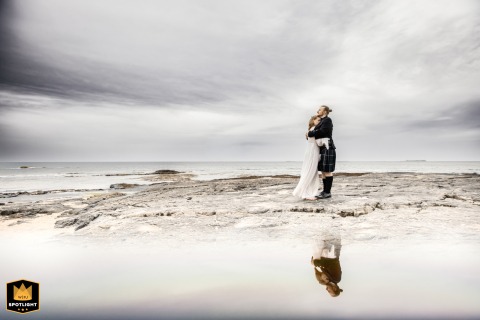 Couple Embraces On A Windswept Shore At Bamburgh Beach In Northumberland, England On Bamburgh Beach, Northumberland, UK, the couple embraces tightly on the rugged, windswept shore, their bond evident against the wild coastal backdrop.