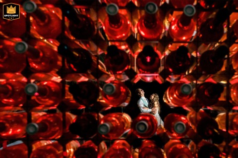   The wedding venue in Zuid Holland provides a creative backdrop as the bride and groom are artistically framed through red wine bottles in an imaginative composition.