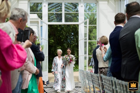 Bride Walks Beside Her Mother Toward Ceremony At Gunnersbury Park In London, England At Gunnersbury Park in London, the bride, accompanied by her mother, arrives at the ceremony, anticipation and emotion marking their meaningful walk together.