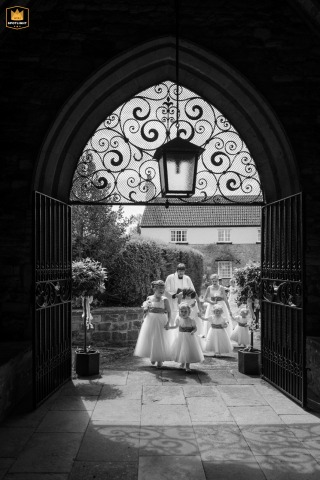   Young flower girls walk together through the ornate entrance of Whissendine village church, their excitement echoed in the stunning backdrop of the historic building.