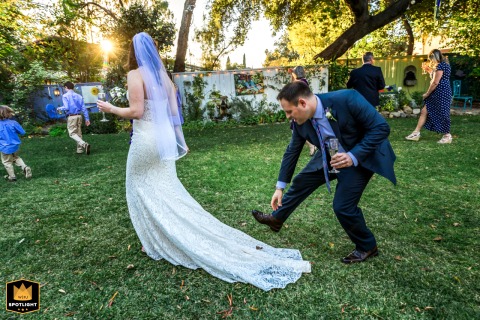   At Lavender Inn in Ojai, CA, the groom gently brushes leaves from the bride's dress as she walks toward her family, a small but caring gesture during the celebration.