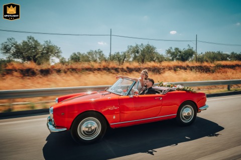 Traveling the roads of Puglia, Italy, the newlyweds ride with the wind in their hair in a vintage red Alfa Romeo, their journey symbolizing freedom and adventure on their wedding day.