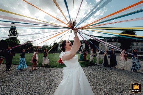 Surrounded by friends at Chateau de Mesnieres en Bray in Normandy, France, the bride joins in the ribbon game, celebrating with a joyful group of girls with her.