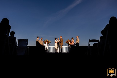 As the ceremony begins in Plymouth, Massachusetts, witnesses are silhouetted, their presence gently framing the heartfelt exchange of vows at the altar.