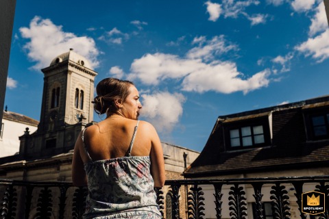 On a balcony in Brighton, UK, a bridesmaid leisurely vapes, her exhaled clouds playfully rising into the sky, creating an artistic interaction with the open air and cityscape.