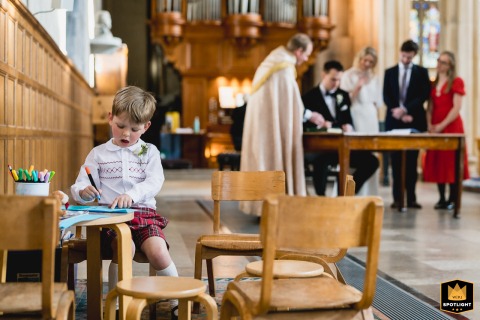 Inside the Barbican in London, a little boy colors intently in the foreground while the newly married couple signs their marriage contract just behind him.