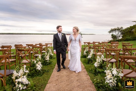 Couple Walks Hand In Hand Through The Countryside Scenery On A Farm In Santa Fe The bride and groom walk hand in hand through the ceremony site on a farm in Argentina, immersed in the afterglow of their vows and the countryside scenery.