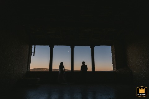The shadow of a couple stretches across the ground at sunset in Provence, France, with vivid colors painting the sky behind their silhouetted forms.
