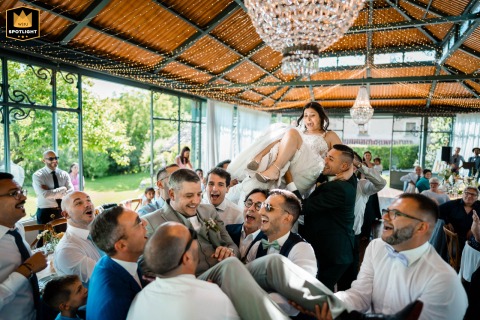 Friends joyfully toss the newlyweds into the air during a lively celebration in the dining room at Mulino dell'olio, Clivio, creating an atmosphere full of cheer and excitement.