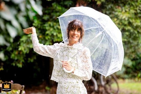 At Chez Ernest in Montauban, a bride beams with a radiant smile under her umbrella, unfazed by the rain, bringing cheerful energy to her wedding day despite the weather.