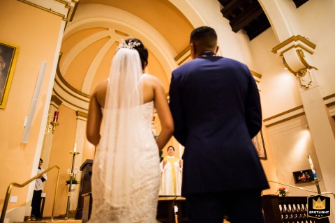 During the ceremony at St. Michael Catholic Church in Livermore, CA, the couple stands at the altar with the officiant in view, as seen from behind for a timeless perspective.