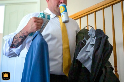   A groomsman descends the staircase at a private house in Ventura, CA, humorously juggling multiple items including his drink, preparing for the wedding festivities underway.