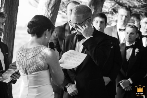 Groom Wipes Away A Tear During Emotional Wedding Vows At Cypress Grove In Mendocino California The groom wipes away a tear at Cypress Grove in Mendocino, CA, showing deep emotion as he listens to his bride read her heartfelt wedding vows during their outdoor ceremony under the trees.