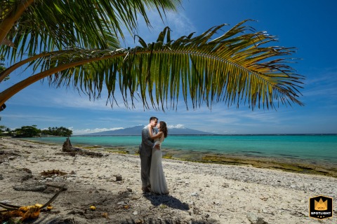 On Tema'e Beach, Moorea, in French Polynesia, the couple share a tender kiss, shielded by a palm leaf while gentle ocean waves complete their romantic session.