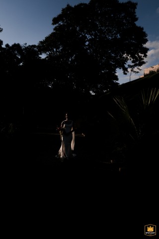 Dappled in tree shadows in São Paulo, the bride stands for a vertical portrait, the natural light and patterns adding an artistic touch to her tranquil demeanor.