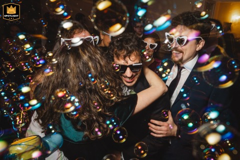 Smiles and energy fill the venue at Vigna Chinet in Turin, Italy, as the groom enthusiastically participates in the wedding festivities while surrounded by friends in sunglasses, and flying bubbles.
