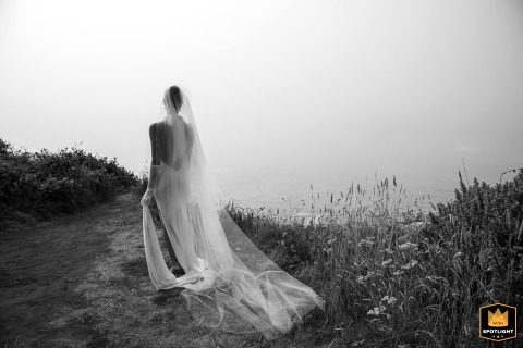 Bride Gazes Over Big River Beach Amid Coastal Fog at MacCallum House in Mendocino, California Enveloped in dense coastal fog at MacCallum House in Mendocino, a bride gazes over Big River Beach, pausing for reflection following her ceremony at Mendocino Land Trust.
