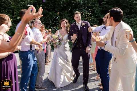 Radiating joy, the bride and groom are welcomed by cheering guests who celebrate enthusiastically as the couple walks between them at their ceremony location in Zug, Switzerland.
