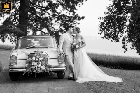 The bride and groom kiss while leaning on the stylish wedding car outside the picturesque Schlössli Utenberg in Luzern, Switzerland.