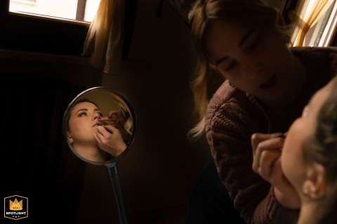 Reflected in a small handheld mirror, a makeup artist carefully applies lipstick to the bride during her wedding preparations at a private home in Gorgo, Mantova, located in Italy.
