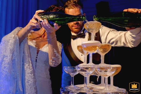 Joyful Newlyweds Pop Open Champagne Bottles To Pour Into A Grand Tower Tower At Domaine De Suzel France At Domaine de Suzel in France, the wedding couple joyfully pop open bottles of champagne, pouring into a tower of glasses.
