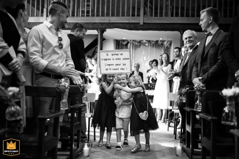Children in formal dress make a synchronized entrance at a church in Haute-Garonne, France, their smiles and playful glances at each other adding a touch of liveliness to the wedding procession.