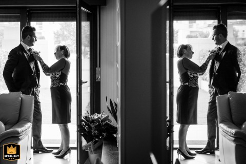 In Udine, Italy, quiet tenderness unfolds as the groom’s mother assists with his buttons, her mindful gesture tracing a familiar, generational rhythm amid the morning’s whirlwind of preparations.