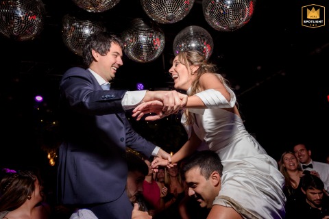 In Funes, Argentina, the bride and groom dance while seated on the shoulders of guests, turning the dance floor into a lively celebration filled with energy and laughter.