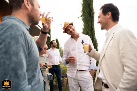 During cocktail hour at Clos du Tuilier in the Luberon region of Provence, France, a group of men stand in near-perfect synchronization, creating a humorous and visually striking scene within the wedding celebration.